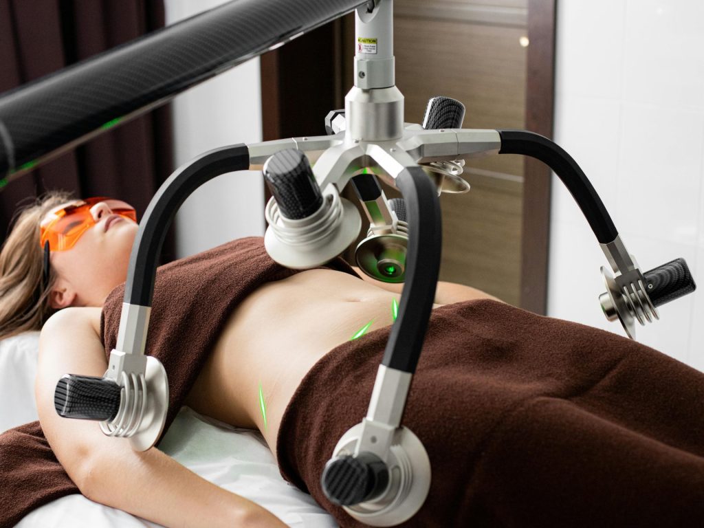 Une patiente est allongée sur une table, sous les lasers d'un appareil moderne de perte de poids appliqués sur son ventre lors d'une liposuccion dans une clinique médicale.